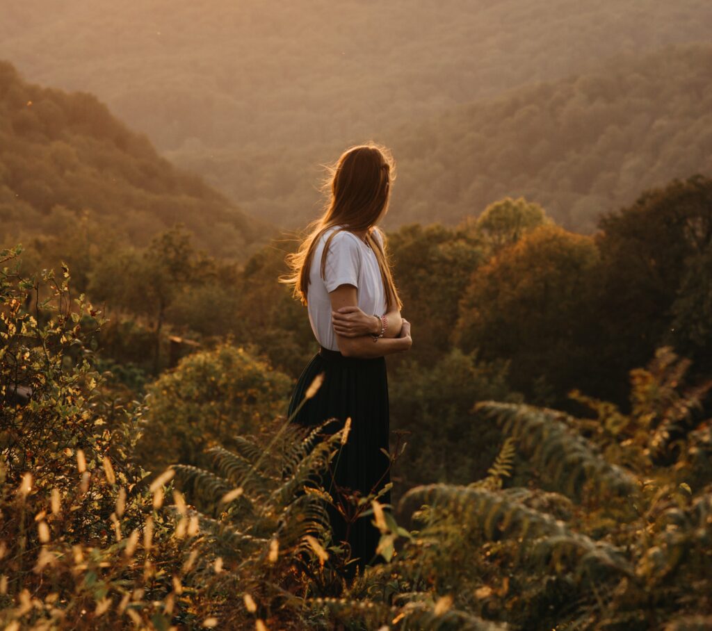 A woman standing among flowers atop a hill at twilight 